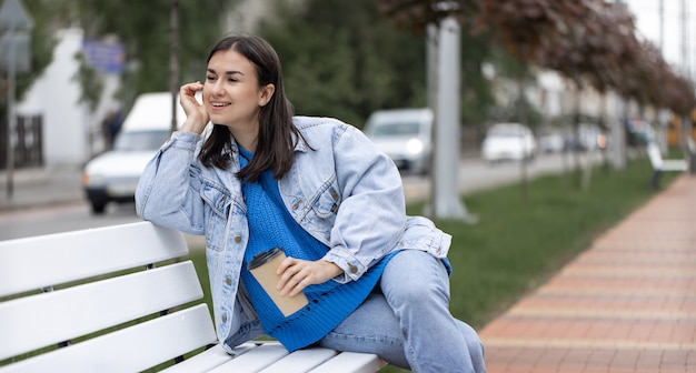 Photo de rue d'une jolie jeune femme assise sur un banc avec un café à la main