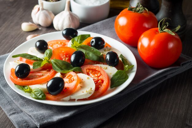 Photo de salade caprese avec tomates, basilic, mozzarella, olives et huile d'olive. Ingrédients de la salade caprese traditionnelle italienne. Concept de cuisine méditerranéenne, biologique et naturelle.