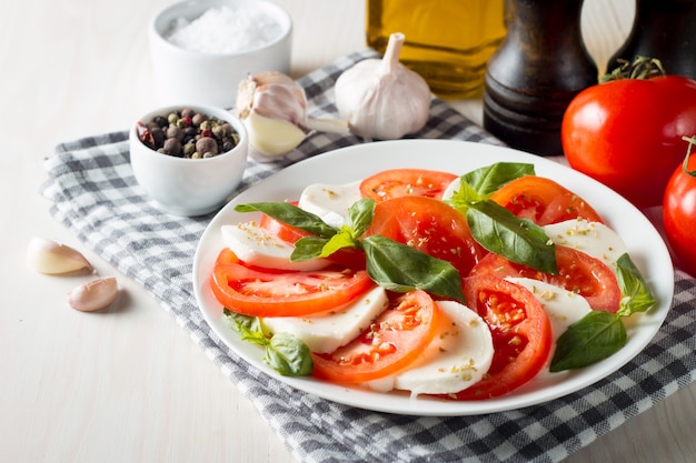 Photo de salade caprese avec tomates, basilic, mozzarella, olives et huile d'olive. Ingrédients de la salade caprese traditionnelle italienne. Concept de cuisine méditerranéenne, biologique et naturelle.