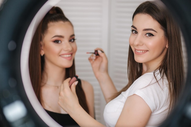 Photo si la lampe annulaire de la maquilleuse fait un maquillage pour une jolie jeune fille Fond de paravent blanc