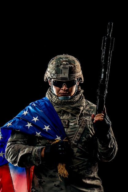 Photo d'un soldat tenant le drapeau américain en arrière-plan. Soldat des forces spéciales des États-Unis ou entrepreneurs militaires tenant un fusil. Image sur fond. concept de soldat, d'armée, de guerre, d'arme et de technologie.