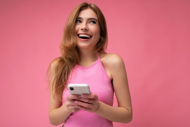 Photo de sourire heureux bien à la jeune femme blonde portant haut rose empoisonnement isolé sur rose