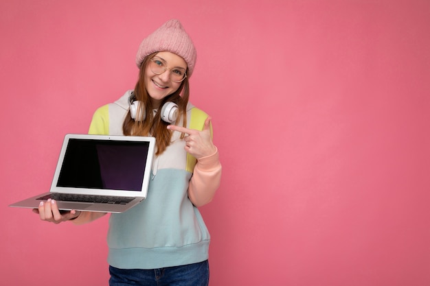 Photo de sourire heureux charmant jolie jeune femme portant chapeau chandail coloré et lunettes tenant