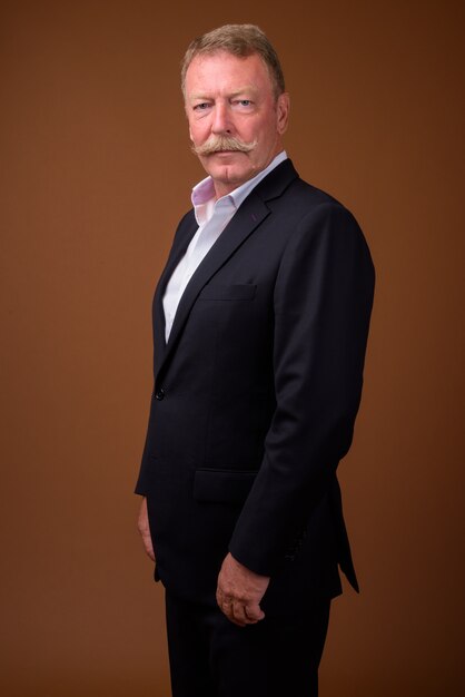 Photo de Studio de bel homme d'affaires senior avec moustache contre brown