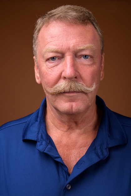 Photo de Studio de bel homme senior avec moustache portant un polo bleu contre brown