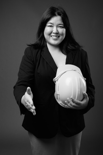 Photo de Studio de belle femme d'affaires asiatique en surpoids tenant un casque sur fond gris en noir et blanc