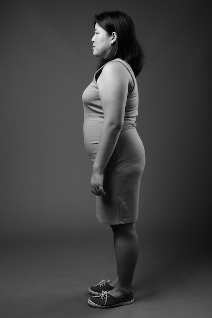 Photo de Studio de belle femme asiatique en surpoids portant une robe sans manches sur fond gris en noir et blanc