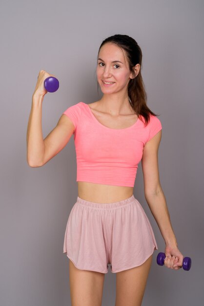 Photo de Studio de belle jeune femme prête pour la salle de sport en souriant et à la recherche de plaisir contre gris