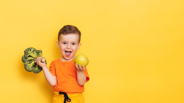 Une photo de studio d'un garçon tenant un brocoli frais et une pomme verte.