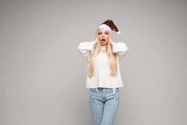 Photo de studio en gros plan d'une belle jeune femme en bonnet de Noel mettant les mains autour de la bouche et faisant des grimaces