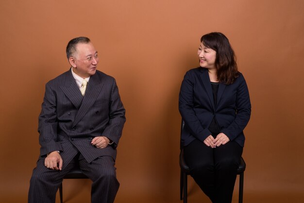 Photo de Studio d'homme d'affaires japonais mature et femme d'affaires japonaise mature ensemble sur fond marron