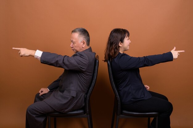 Photo de Studio d'homme d'affaires japonais mature et femme d'affaires japonaise mature ensemble sur fond marron