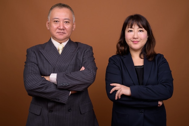 Photo de Studio d'homme d'affaires japonais mature et femme d'affaires japonaise mature ensemble sur fond marron