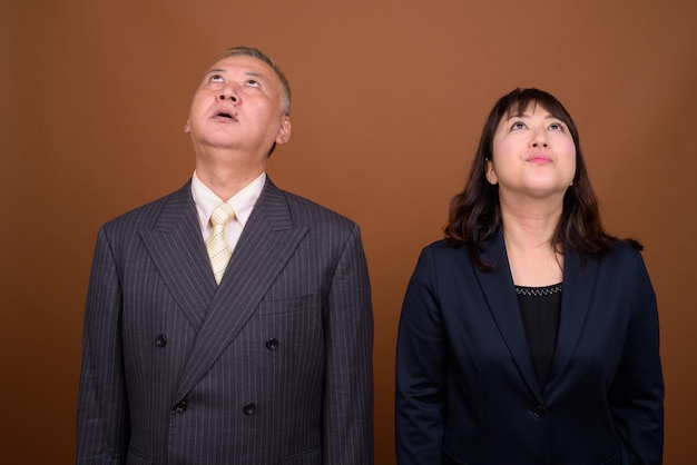 Photo de Studio d'homme d'affaires japonais mature et femme d'affaires japonaise mature ensemble sur fond marron