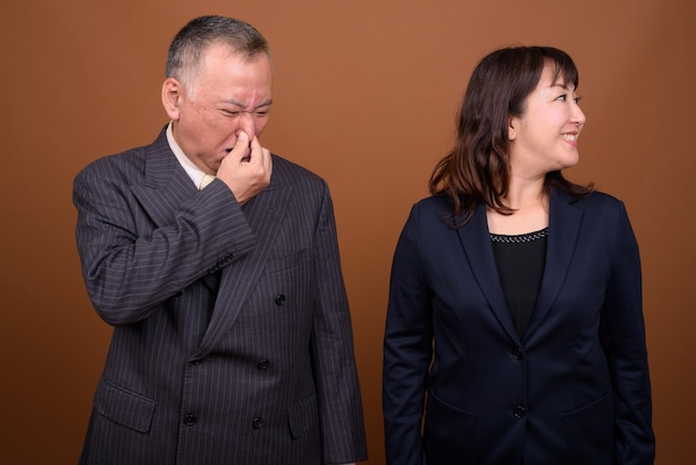 Photo de Studio d'homme d'affaires japonais mature et femme d'affaires japonaise mature ensemble sur fond marron