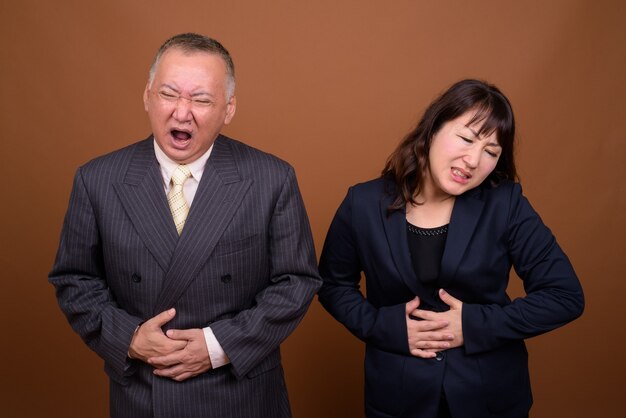 Photo de Studio d'homme d'affaires japonais mature et femme d'affaires japonaise mature ensemble sur fond marron