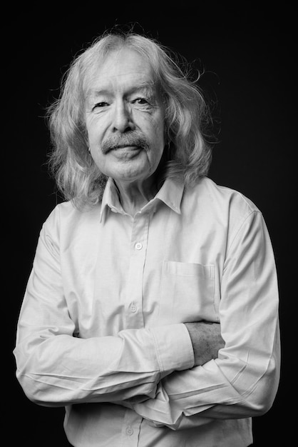 Photo de studio d'un homme d'affaires senior avec une moustache portant une chemise rose contre un mur gris