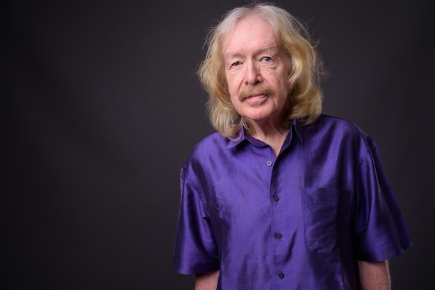 Photo de Studio d'un homme senior avec moustache portant une chemise soyeuse violette sur fond gris