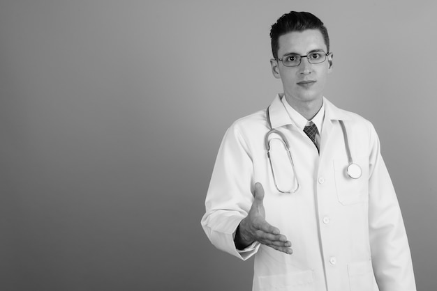 Photo de Studio de jeune bel homme médecin portant des lunettes sur fond gris en noir et blanc