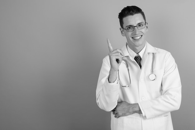 Photo de Studio de jeune bel homme médecin portant des lunettes sur fond gris en noir et blanc