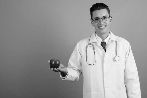 Photo de Studio de jeune bel homme médecin portant des lunettes sur fond gris en noir et blanc