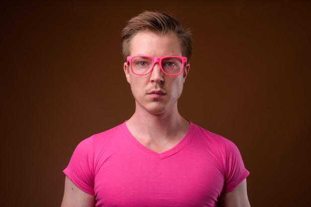 Photo de Studio de jeune bel homme portant une chemise rose avec des lunettes roses assorties sur fond marron