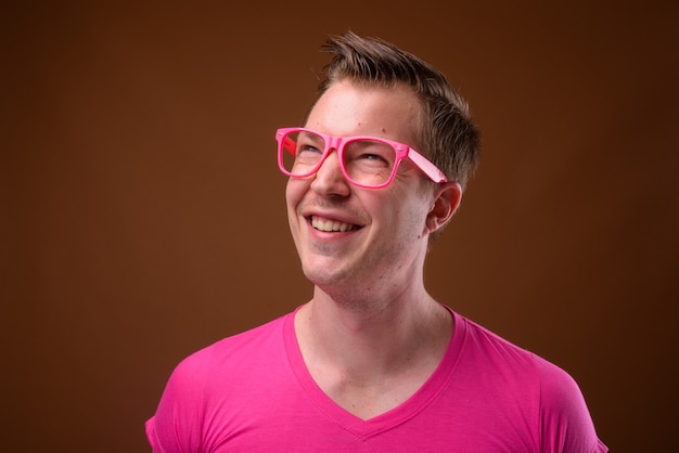 Photo de Studio de jeune bel homme portant une chemise rose avec des lunettes roses assorties sur fond marron