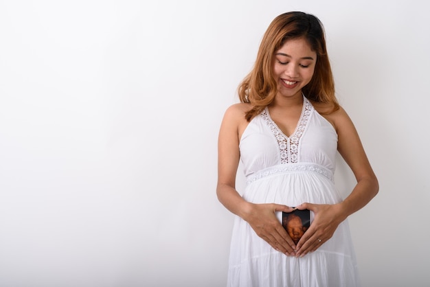 Photo de Studio de jeune femme enceinte asiatique heureuse souriant et regarde