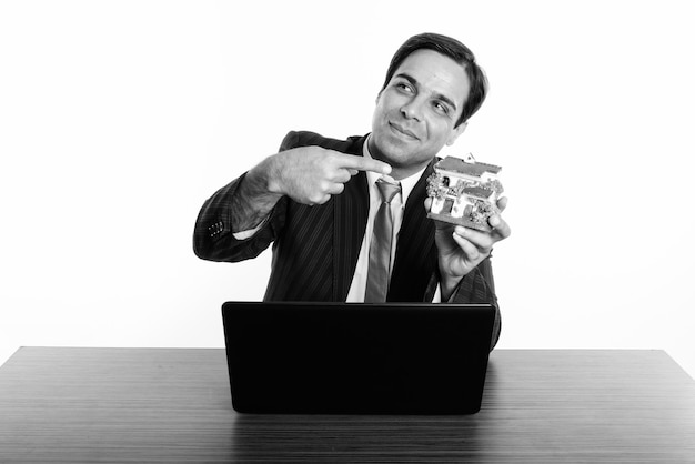 Photo de Studio de jeune homme d'affaires persan assis derrière un bureau en bois isolé, noir et blanc