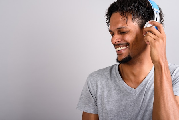 Photo de Studio de jeune homme africain beau barbu, écouter de la musique sur fond gris