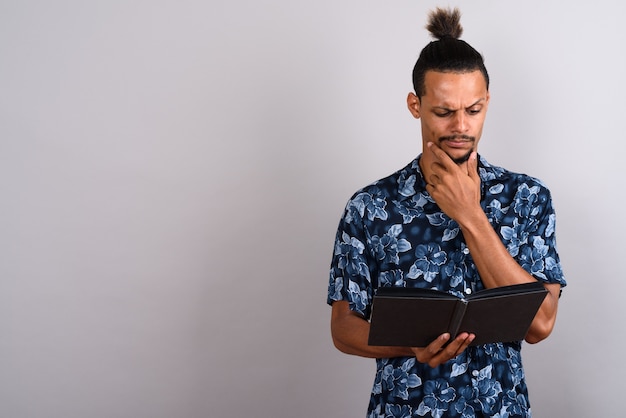 Photo de Studio de jeune homme africain beau barbu livre de lecture sur fond gris