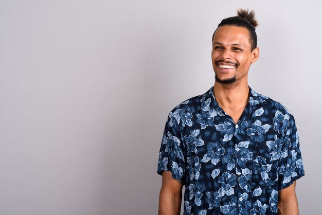 Photo de Studio de jeune homme africain beau barbu portant une chemise hawaïenne avec les cheveux attachés sur fond gris