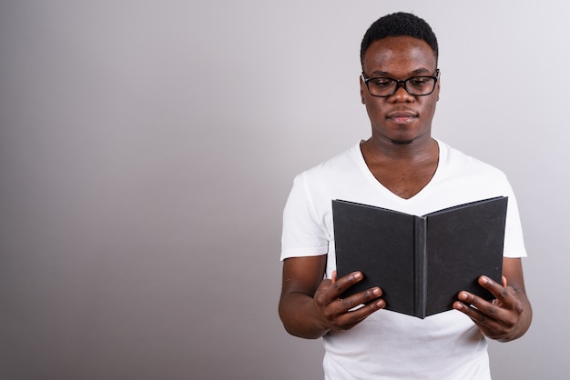 Photo de Studio de jeune homme africain portant des lunettes tout en lisant un livre sur fond blanc