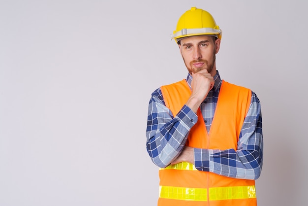 Photo de Studio de jeune homme barbu ouvrier contre blanc