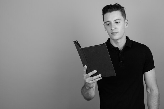 Photo de Studio de jeune homme beau livre de lecture sur fond gris en noir et blanc