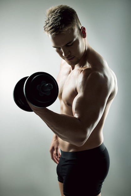 Photo de studio d'un jeune homme musclé faisant de l'exercice avec un haltère sur un fond gris