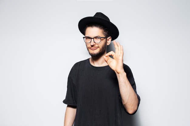 Photo de studio d'un jeune homme séduisant gesticulant le signe OK portant un chapeau noir