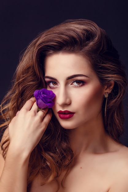 Photo de studio de mode de belle femme brune avec un maquillage lumineux avec un bouquet d'eustoma violet et blanc