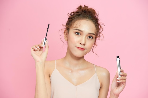 Photo de studio de mode de belle jeune femme avec un maquillage lumineux tenant le mascara à la main