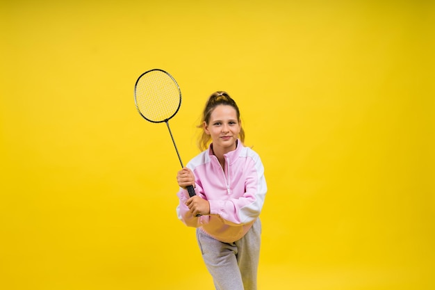 Photo studio pleine longueur d'une fillette de dix ans tenant une raquette de badminton et isolée sur jaune