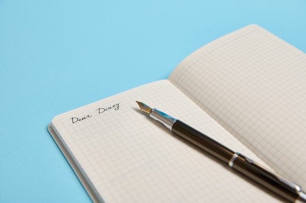 Photo de studio recadrée d'un bloc-notes ouvert avec le mot Cher journal et un stylo à encre isolé sur fond bleu avec espace de copie pour le texte