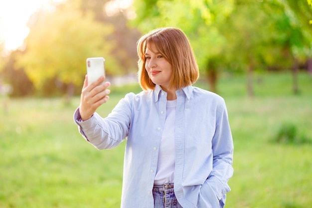 Photo d'une superbe dame à la coiffure ondulée positive faisant un enregistrement de selfie vidéo soirée coucher de soleil rue