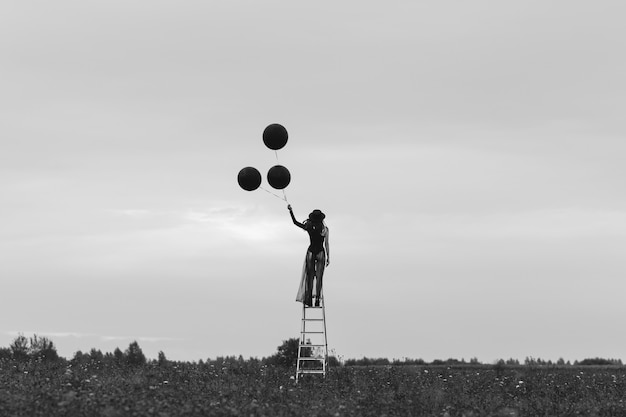 Photo surréaliste d'une fille dans un chapeau avec des ballons à la main dans un champ