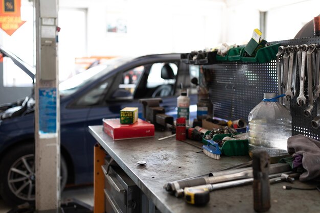 Photo d'une table en métal avec des outils de travail pour travailler et réparer une voiture dans le contexte d'une voiture de tourisme bleue dans une station-service en cours de réparation avec un capot ouvert.