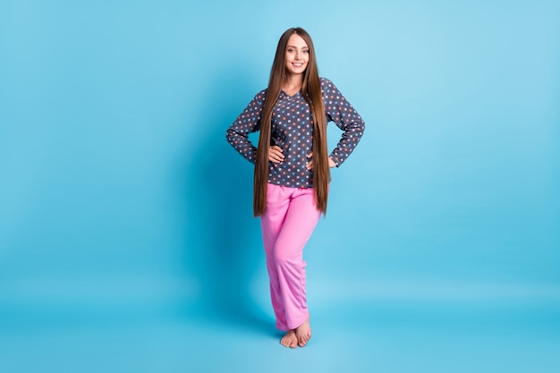 Photo De La Taille Du Corps Entier D'une Charmante Jeune Fille Souriante, Mains, Hanches, Pieds Nus, Préparer Les Procédures Du Matin, Porter Des Pyjamas En Chemise à Pois, Vêtements De Nuit Isolés, Fond De Couleur Bleu Vif