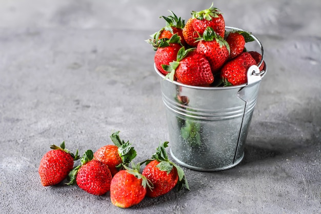 Photo photo de tas de fraises fraîches dans le bol sur fond gris rustique. un tas de fraises mûres dans un bol peut sur la table. copiez l'espace. fruits frais sains. alimentation biologique. nourriture claire