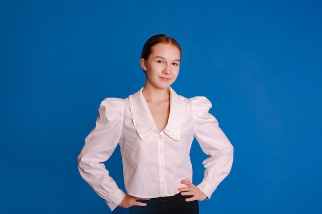 Photo photo de tête d'une adolescente souriante en chemise blanche regardant une caméra isolée sur un fond de studio bleu clair