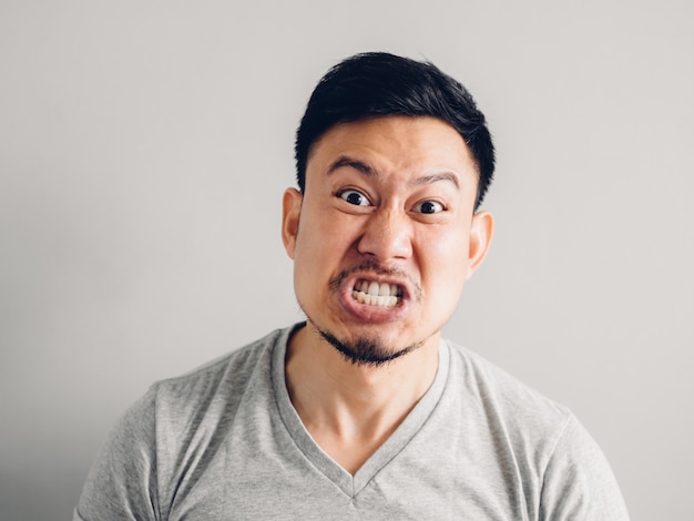 Photo de la tête d&#39;un homme asiatique avec un visage en colère et furieux sur fond gris.