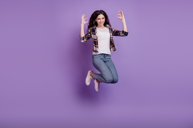 Photo de tout le corps d'une jeune fille séduisante, sourire positif heureux, sauter jusqu'à afficher un signe cool isolé sur fond de couleur violette