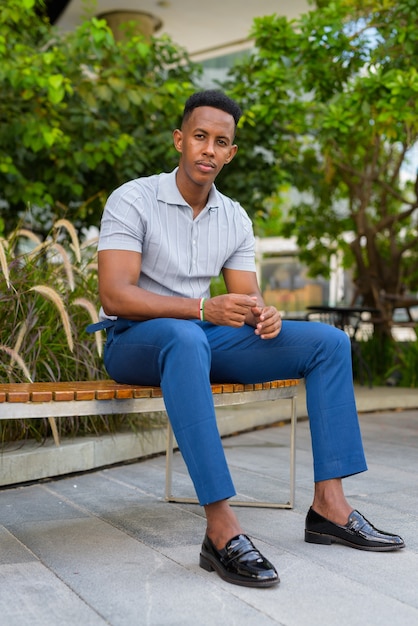 Photo de toute la longueur d'un jeune homme d'affaires africain assis à l'extérieur sur un banc de parc